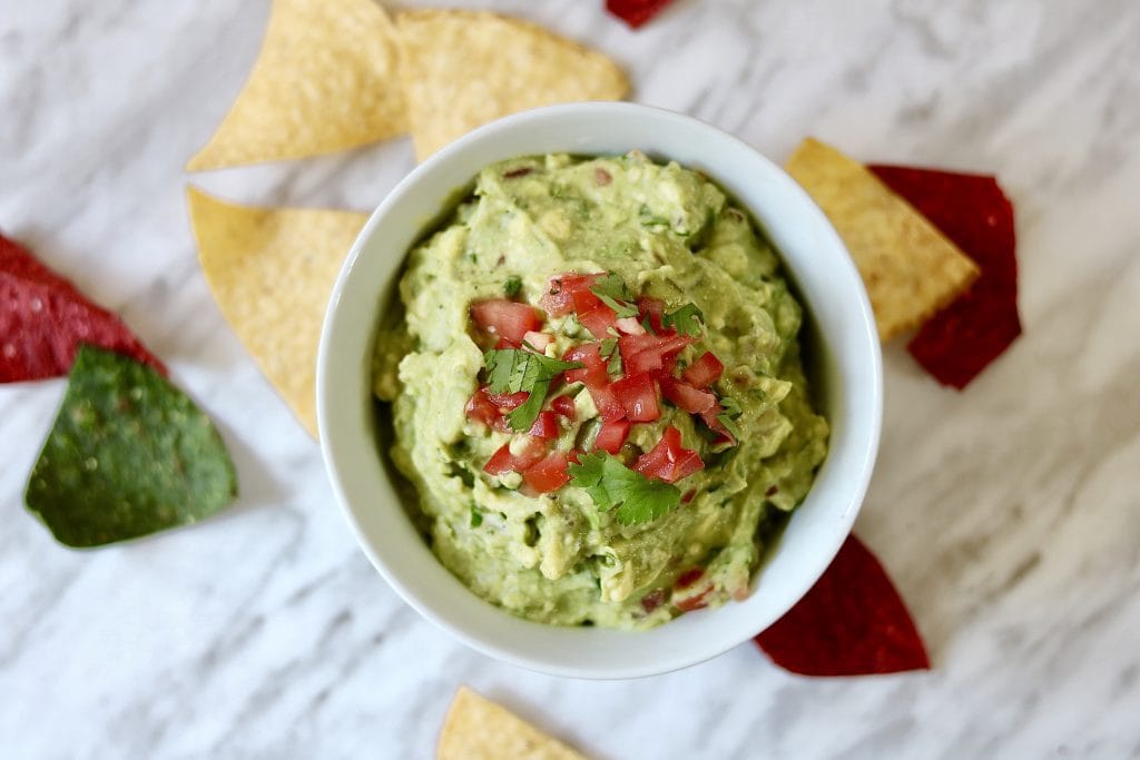 best guacamole recipe in a white bowl on a marble countertop