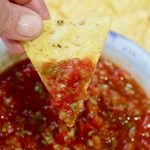 restaurant style salsa in a white bowl with a tortilla chip being dipped
