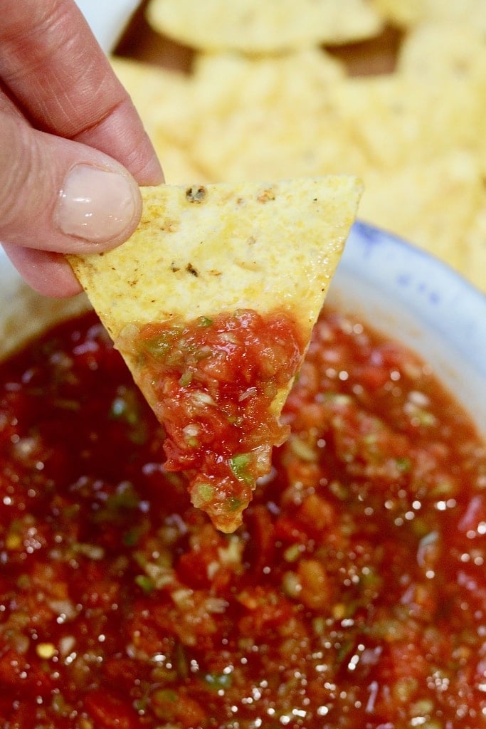 restaurant style salsa in a white bowl with a dipped tortilla chip