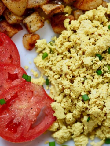 tofu scrambled eggs on a white plate with potatoes and tomatoes