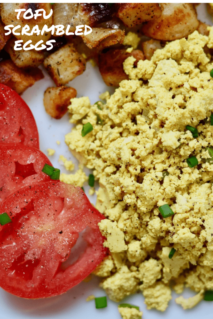 vegan scrambled eggs on a white plate with a fork and tomatoes and potatoes