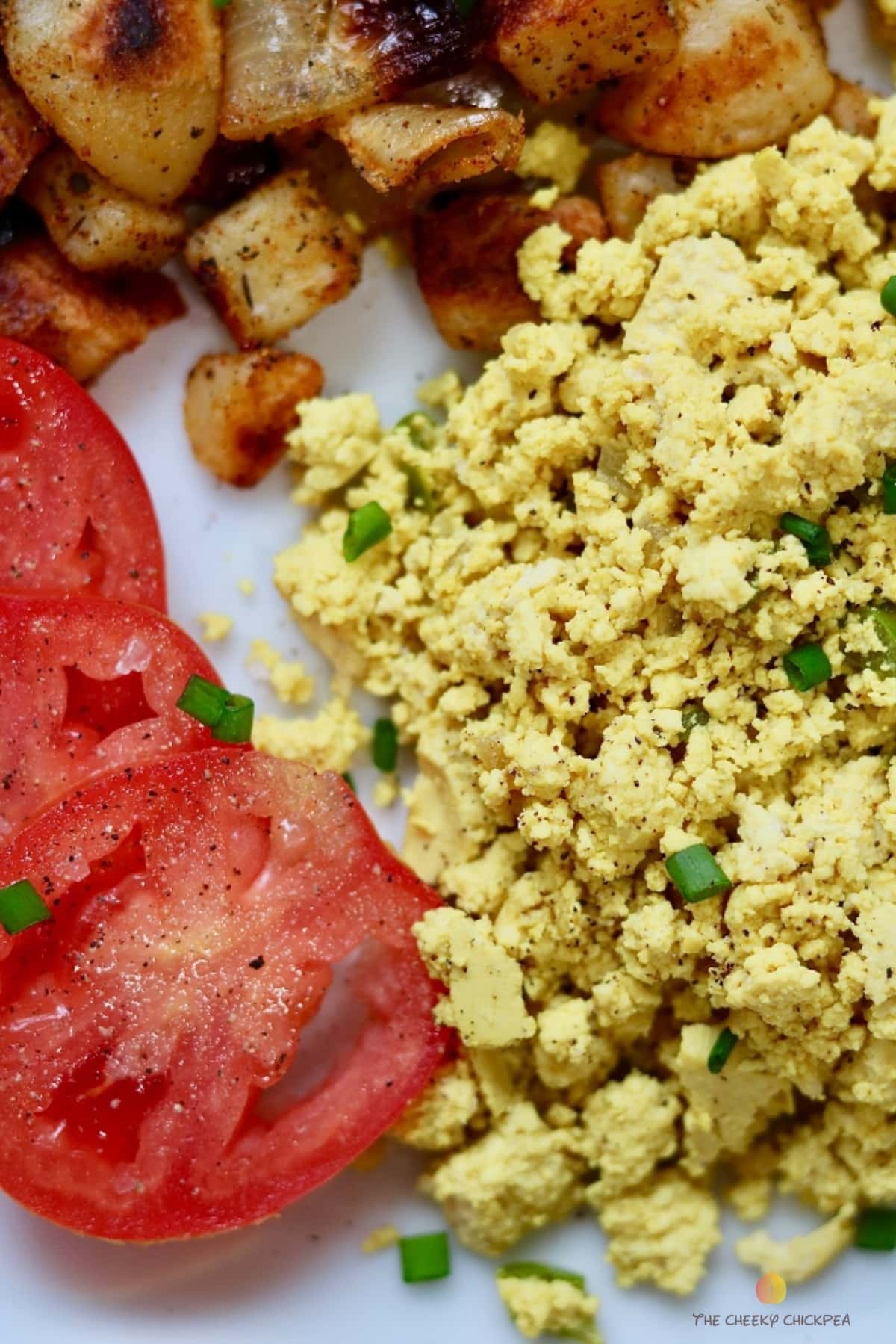 tofu scramble on a white plate with potatoes and tomatoes