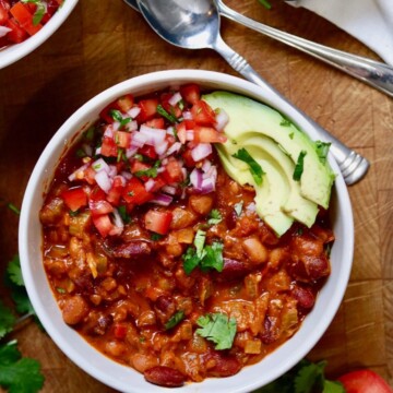 vegan chili in a white bowl with salsa and avocado