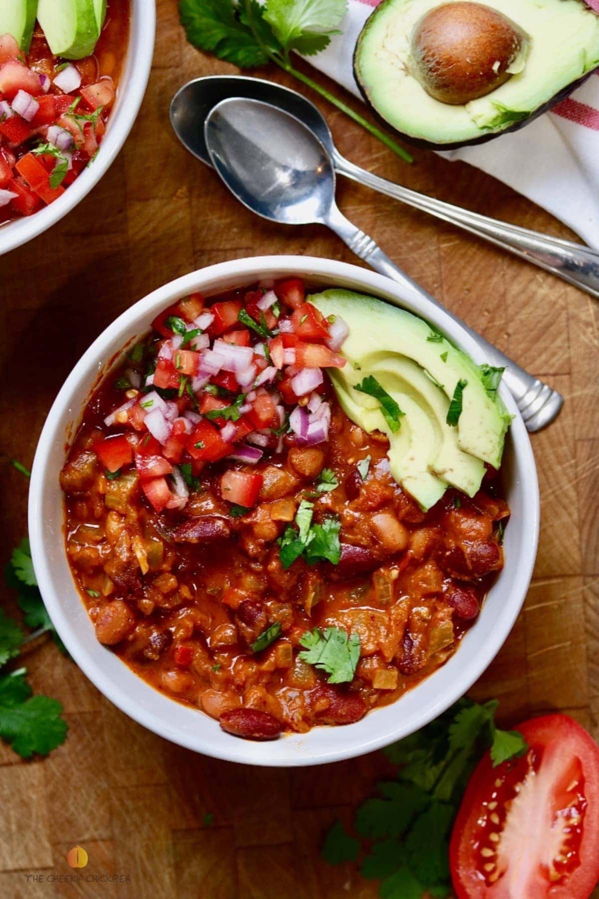 vegan chili in a white bowl with salsa and avocado 