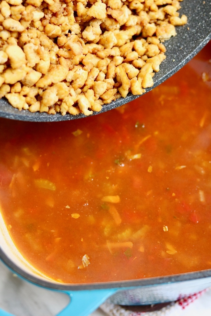 vegan hamburger soup in a pot with tofu crumbles being added