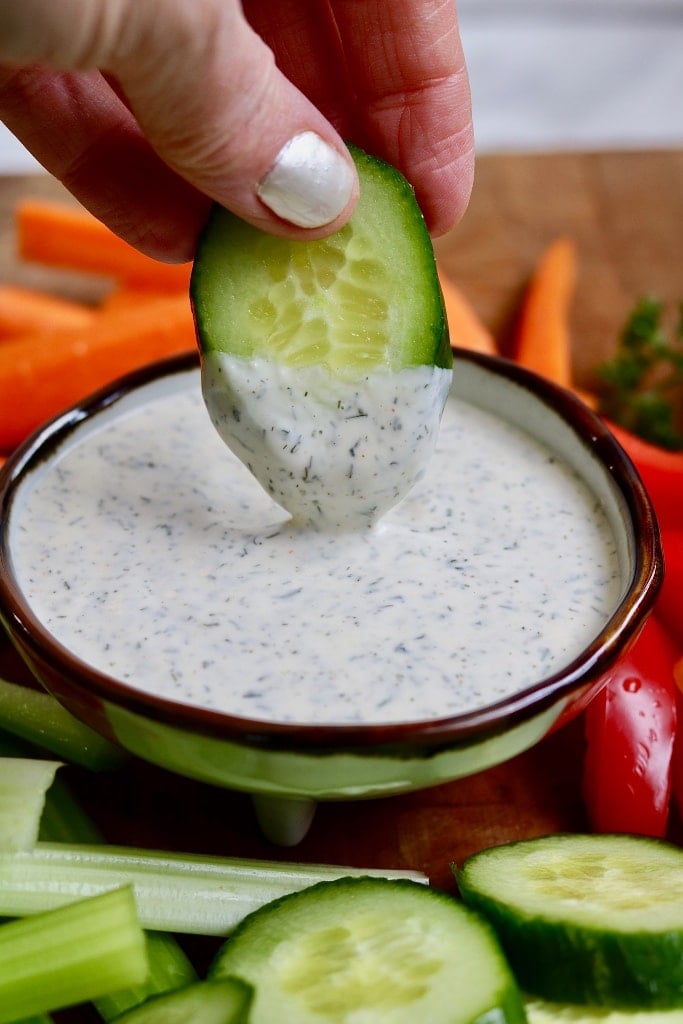 cucumber slice being dipped in a bowl of vegan ranch dressing