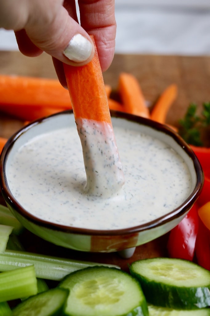 carrot stick being dipped in a bowl of vegan ranch dressing