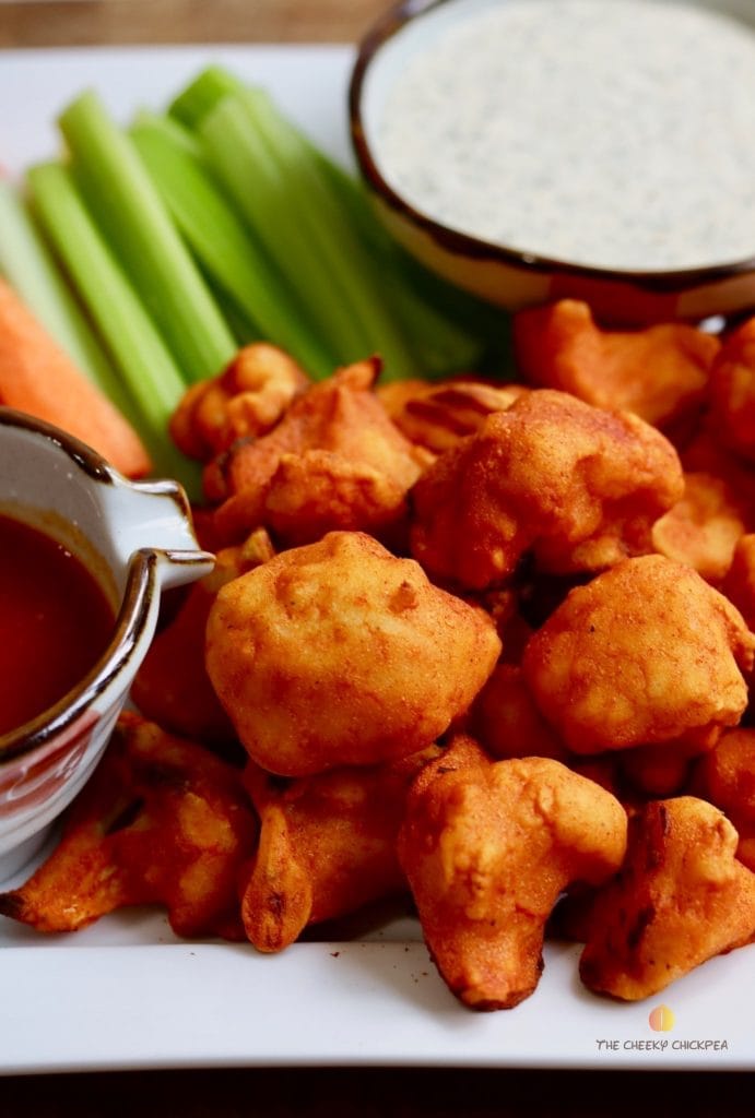 buffalo cauliflower wings on a platter with celery carrots and vegan ranch dressing