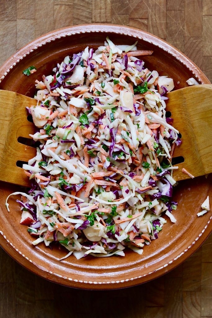 classic vegan coleslaw in a brown bowl with wooden tongs