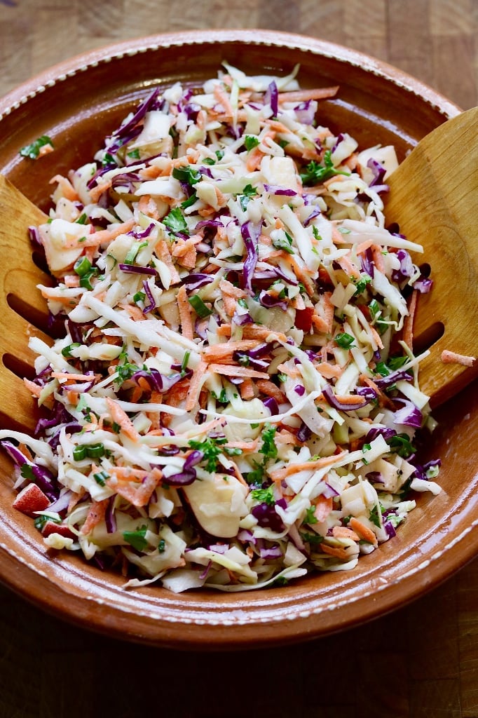 classic vegan coleslaw in a brown bowl with wooden tongs