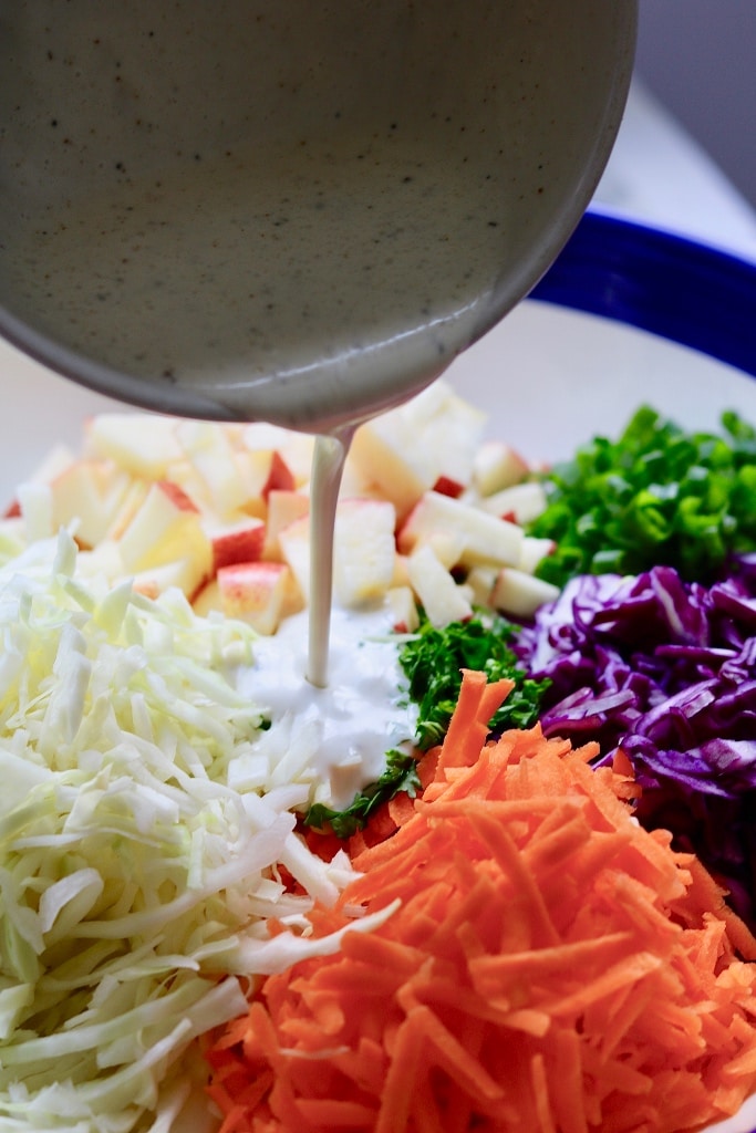 dressing being poured onto classic vegan coleslaw in a white bowl