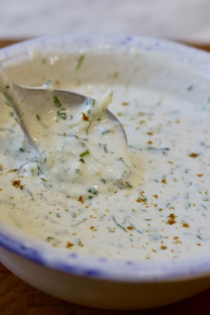 vegan raita in a white bowl with a spoon