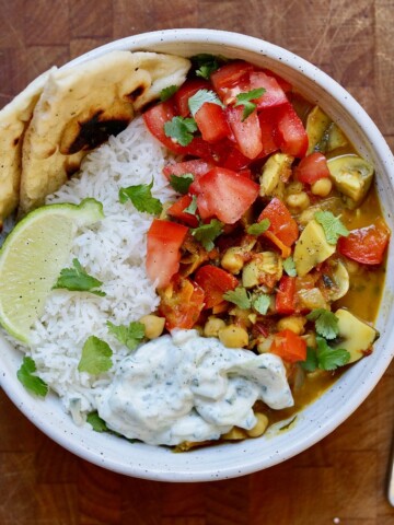 vegetable chickpea curry in a white bowl with rice naan and raita