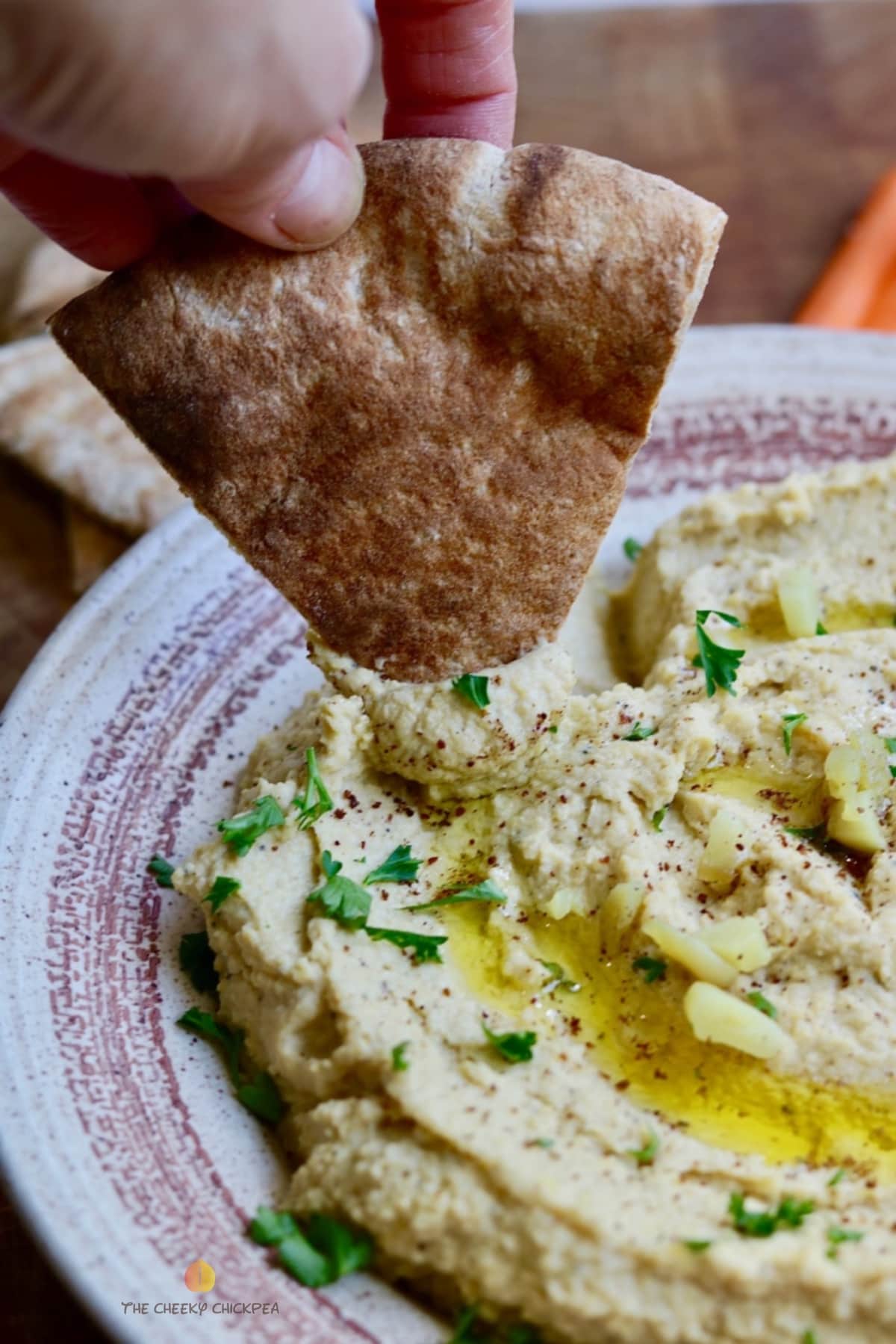 pita bread being dipped in a bowl of homemade hummus