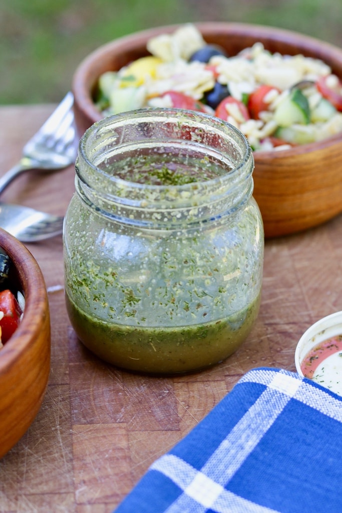 Greek Salad dressing in a glass jar on a wooden cutting board