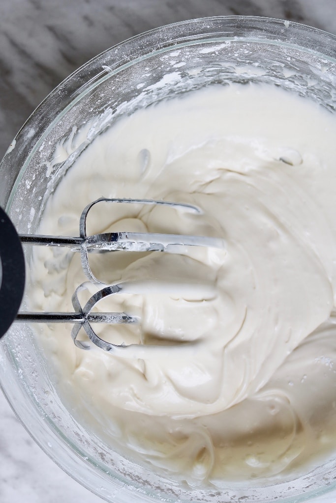 vegan cream cheese frosting being mixed with a hand mixer in a bowl