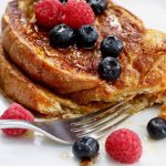 vegan French toast on a white plate with mixed berries and a fork