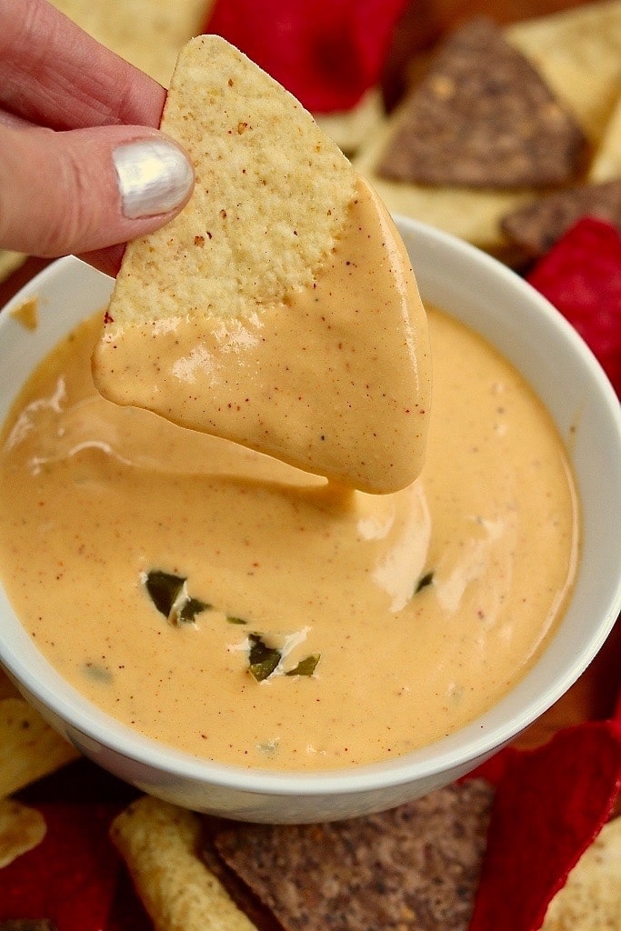 tortilla chip being dipped in vegan nacho cheese sauce