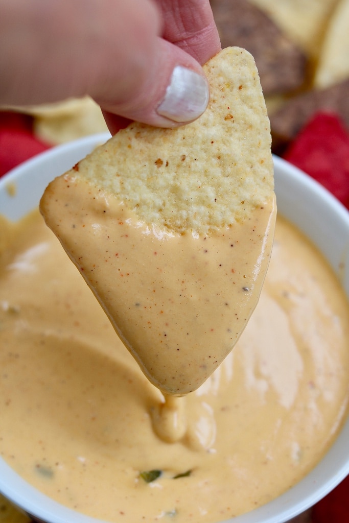 tortilla chip being dipped into vegan nacho cheese sauce
