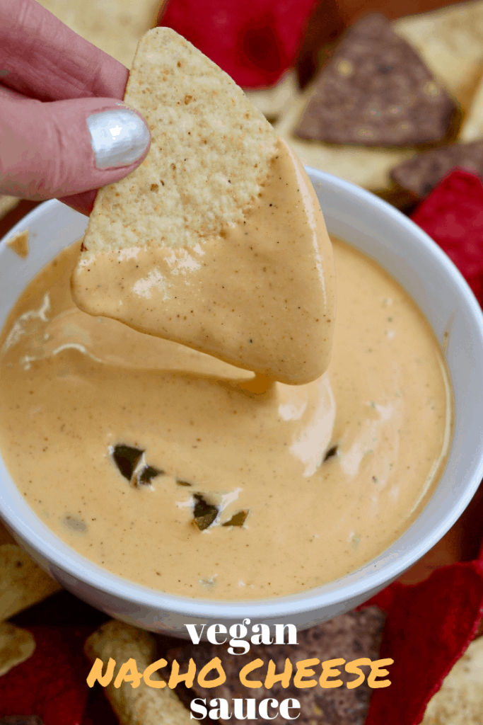 tortilla chip being dipped in vegan nacho cheese sauce