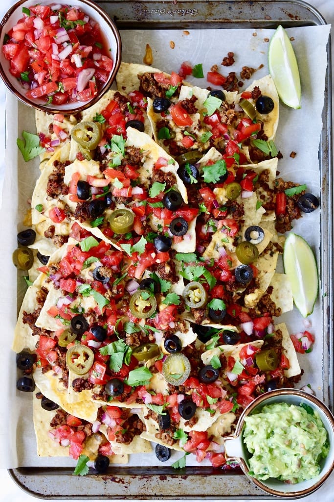 fully loaded vegan nachos on a baking tray with two dips