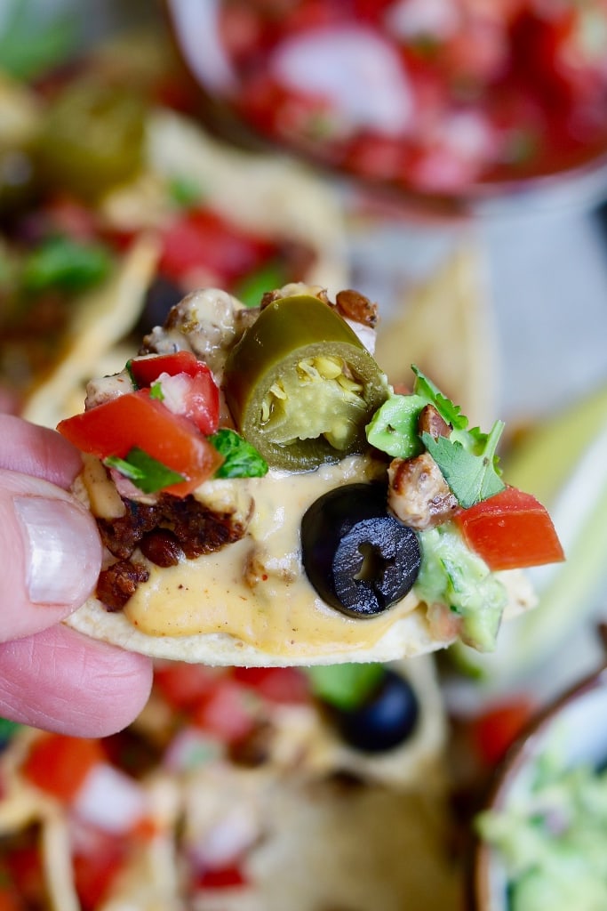 fully loaded vegan nacho chip being held in the air
