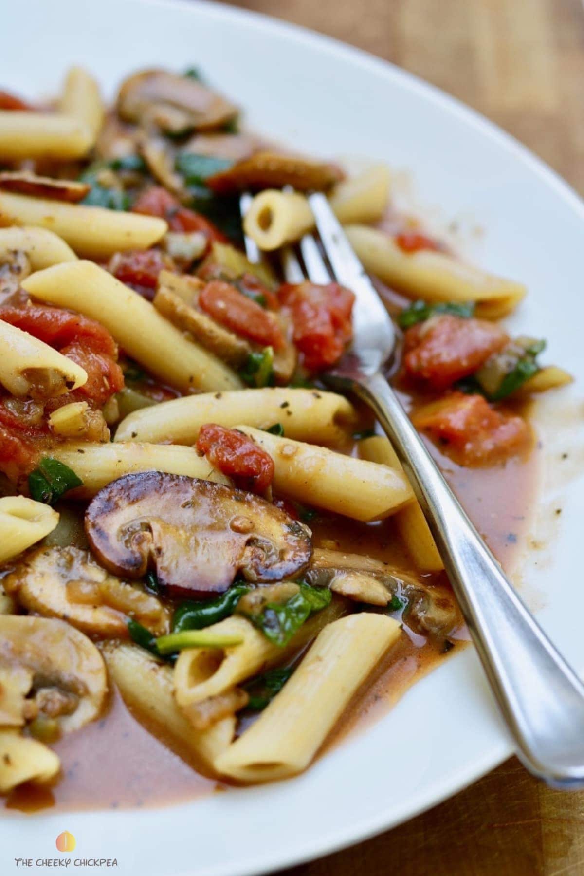 spinach mushroom pasta on a white plate with a fork