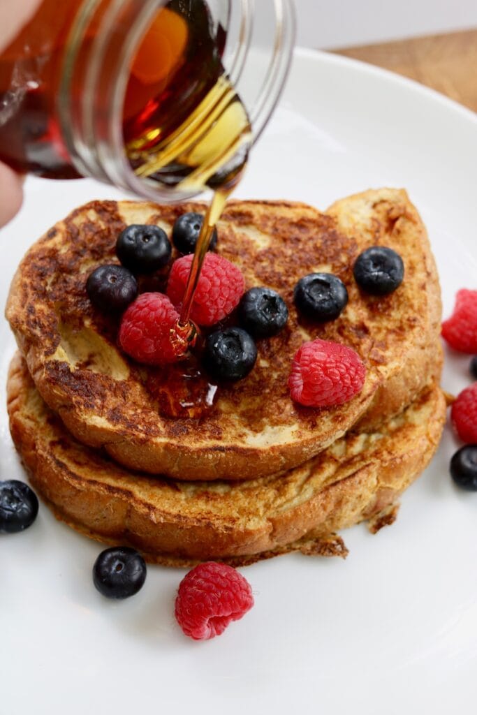 maple syrup being poured over french toast with berries 