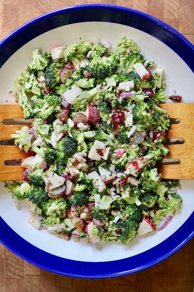vegan broccoli salad in a white and blue bowl with wooden tongs