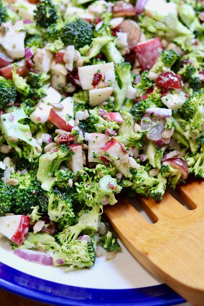 vegan Broccoli Salad in a blue and white bowl with one wooden tong