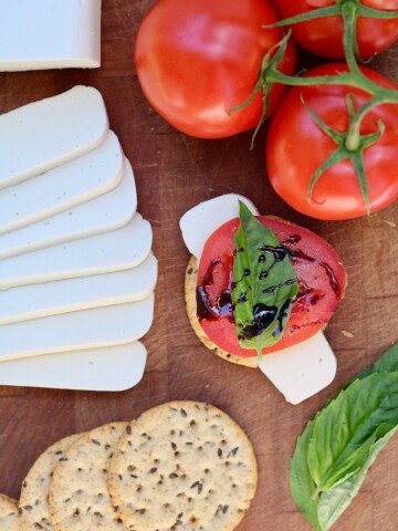 vegan mozzarella sliced on a wooden cutting board with tomatoes and crackers