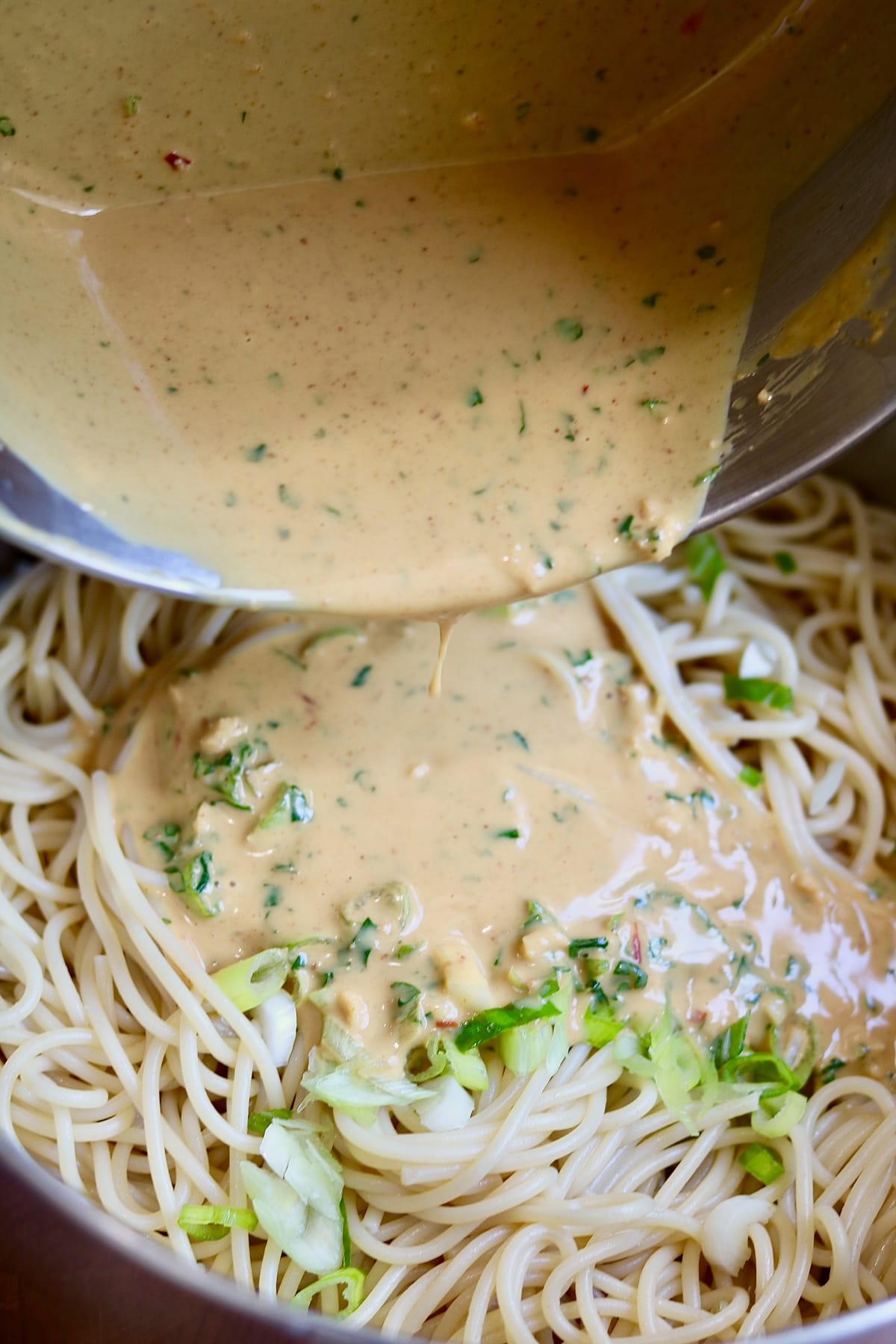 peanut sauce being poured over noodles 