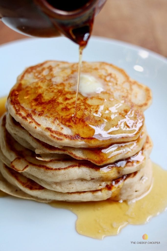 syrup being poured on vegan buttermilk pancakes stacked on a white plate