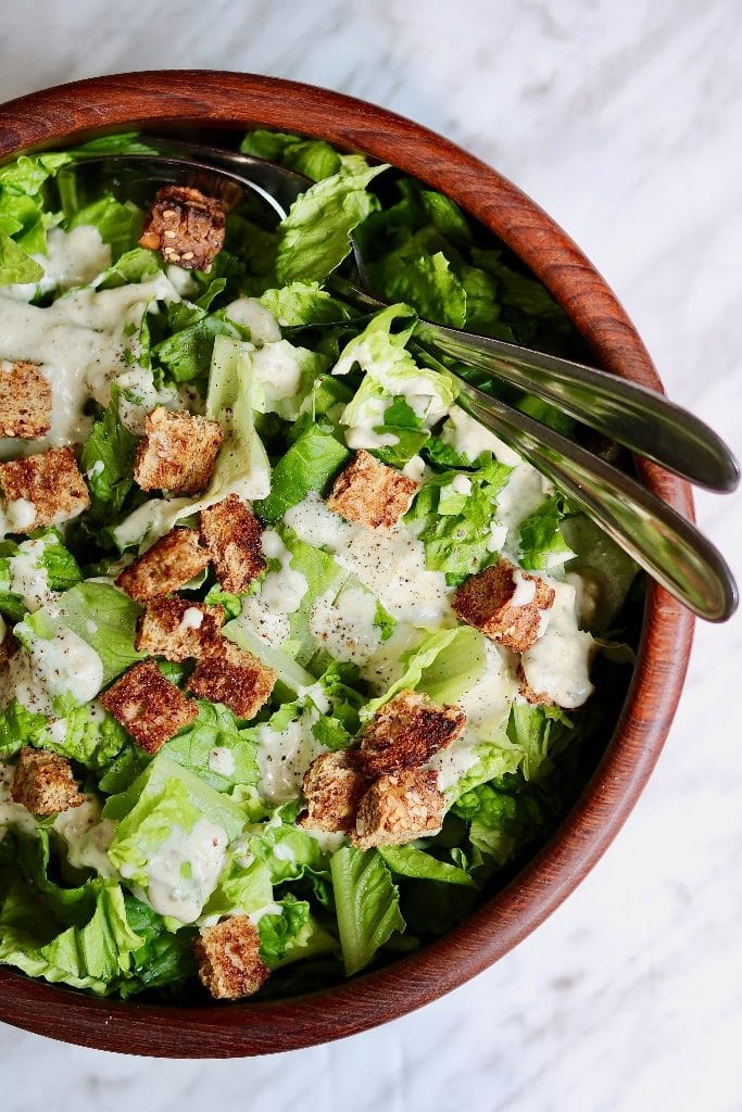 romaine lettuce in a bowl with caesar dressing and croutons