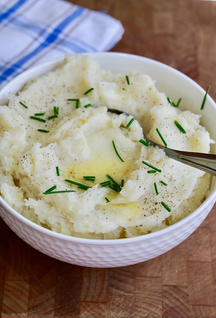 vegan mashed potatoes in a white bowl with melted butter and a spoon