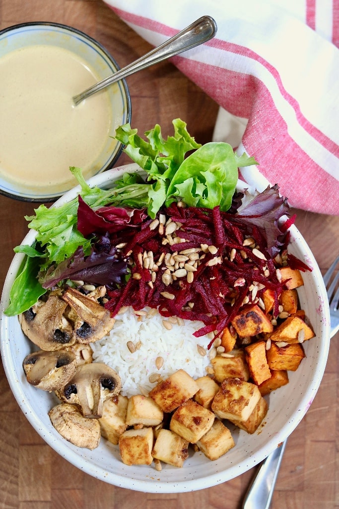 vegan buddha bowl on a wooden counter with a bowl of peanut dressing