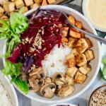 vegan buddha bowl surrounded by bowls of vegetables and tofu