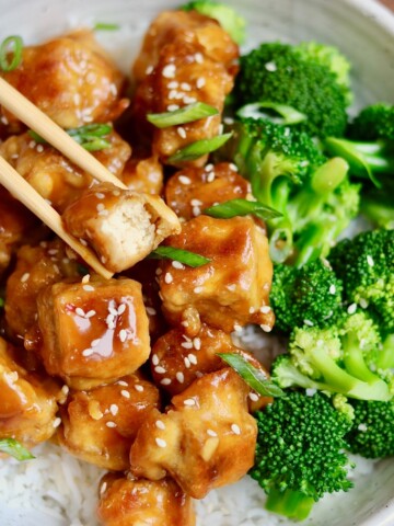 vegan orange chicken in a bowl with broccoli and chopsticks