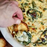 vegan spinach artichoke dip being scooped with sliced baguette