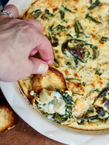 vegan spinach artichoke dip being scooped with sliced baguette