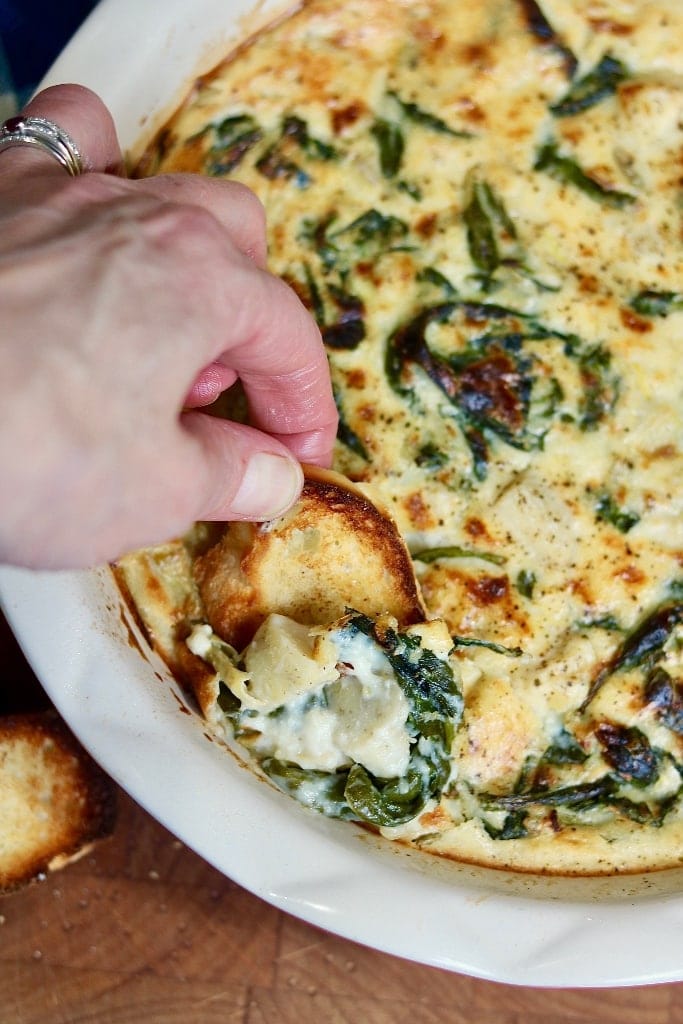 vegan spinach artichoke dip being scooped with sliced baguette 