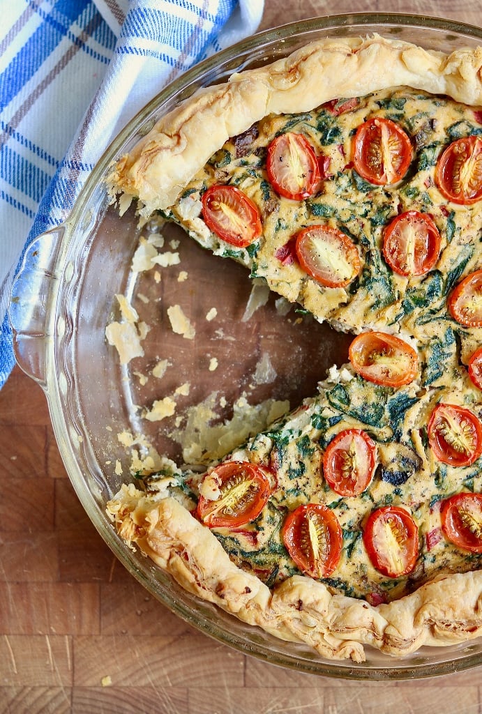 vegan quiche in a pie plate with a slice missing
