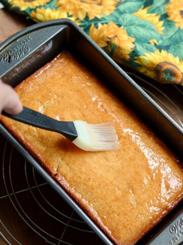 vegan lemon loaf in a pan being brushed with lemon drizzle