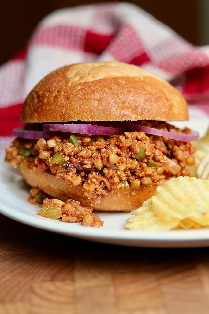 a vegan sloppy Joe bun on a white plate with potato chips 