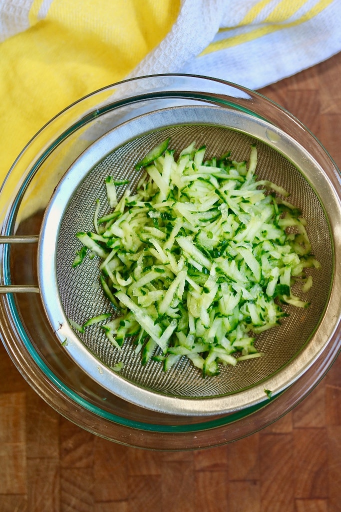 grated cucumber in a strainer over a bowl