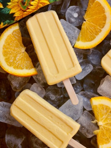 two creamsicles on a bed of ice with orange slices