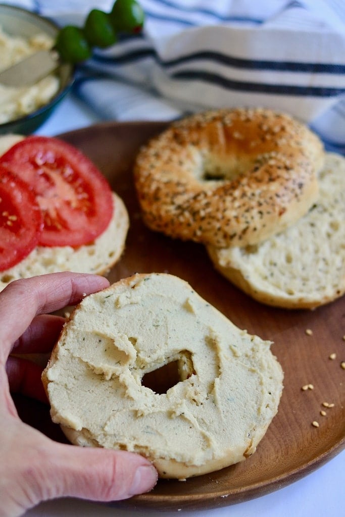 half a bagel with vegan cream cheese being picked up