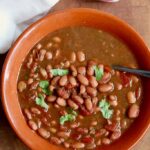 a bowl of charro beans with a spoon