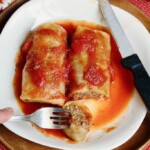 two cabbage rolls on a plate with fork and knife