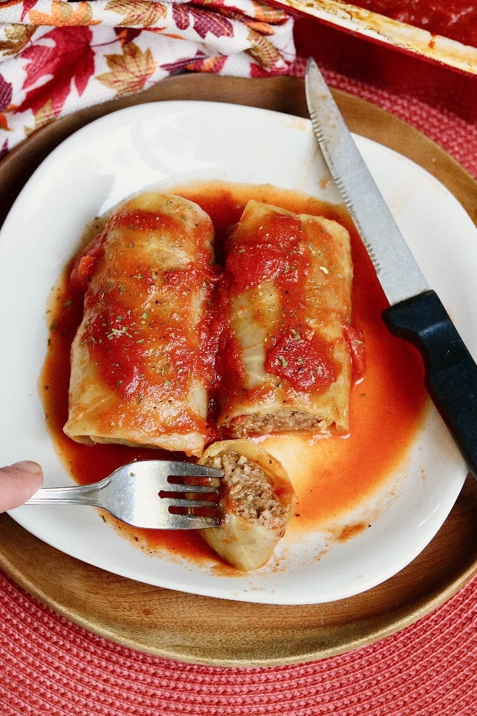 two cabbage rolls on a plate with fork and knife